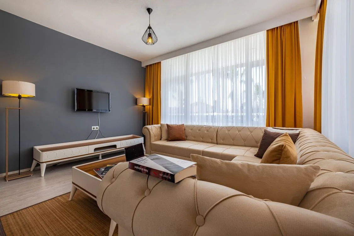 Lichtdurchfluteter Wohnraum mit cremefarbenem Sofa, Gardinen und warmen Textilien